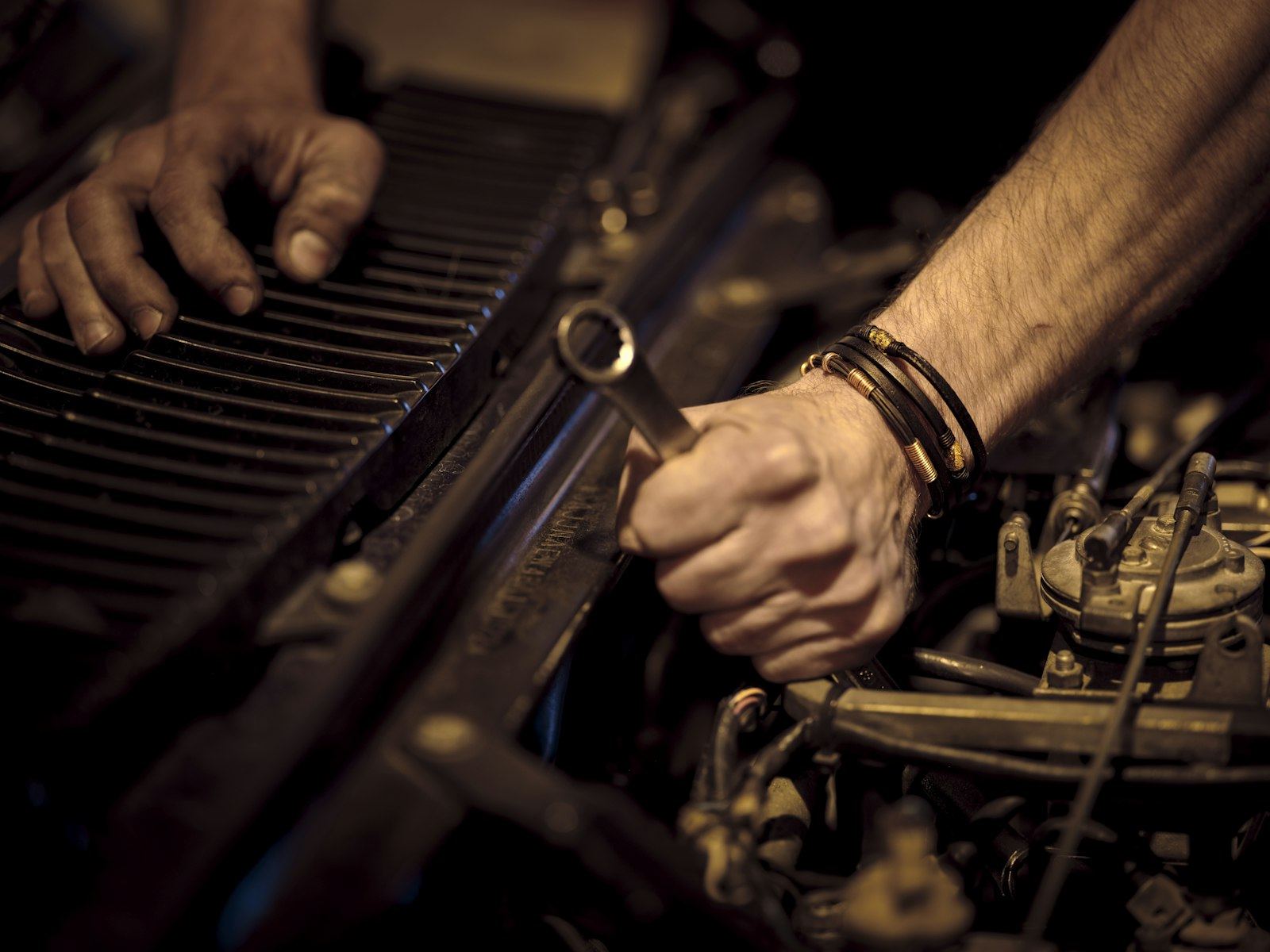 Mãos de mecânico apertando uma peça do motor com chave combinada